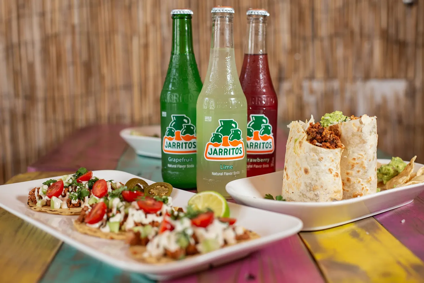Trois tacos, des sodas Jarritos et des quesadillas sur une table colorée du restaurant
